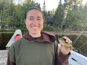 Melissa smiling holding a small fish while standing on a dock